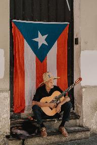 man holding guitar sitting in front of hanged flag